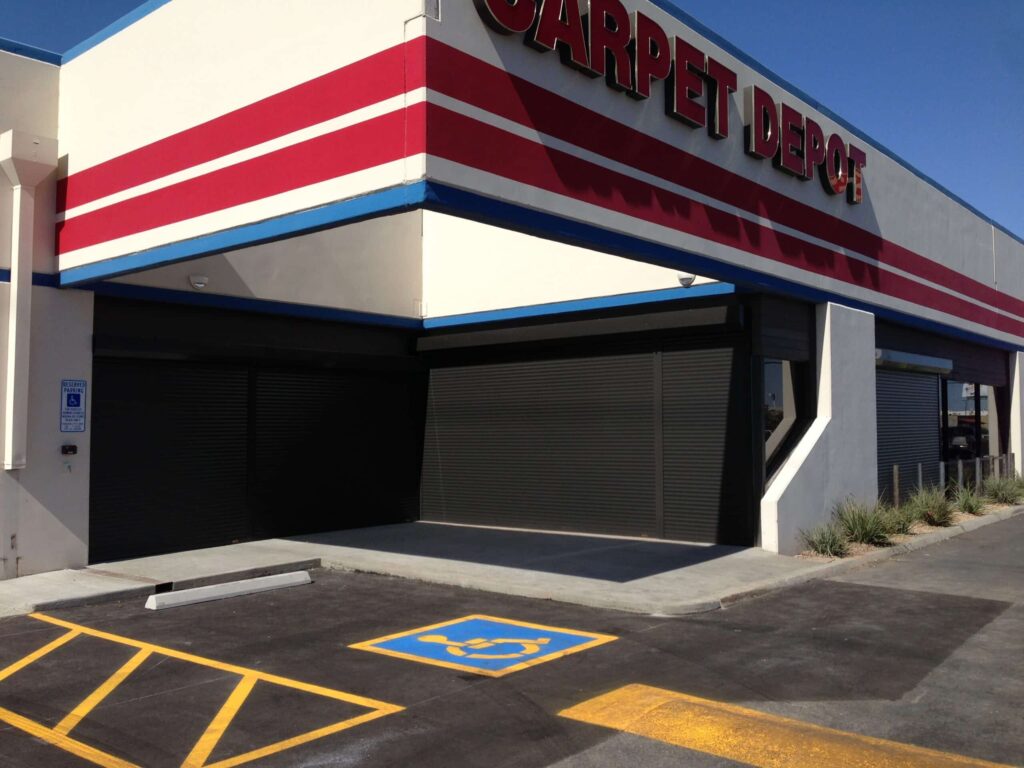 Exterior view of a Carpet Depot building with closed roller shutters. A designated blue parking space for individuals with disabilities is visible in front.