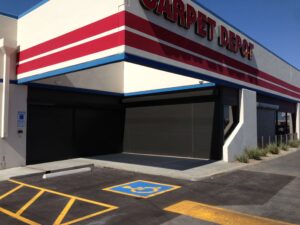 Exterior view of a Carpet Depot building with closed roller shutters. A designated blue parking space for individuals with disabilities is visible in front.