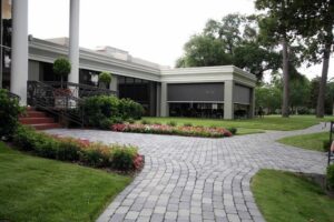 A pathway made of stone leading through a landscaped garden towards a modern building with large windows, surrounded by greenery and flower beds.