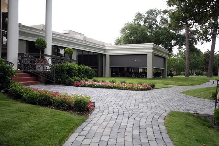 A pathway made of stone leading through a landscaped garden towards a modern building with large windows, surrounded by greenery and flower beds.